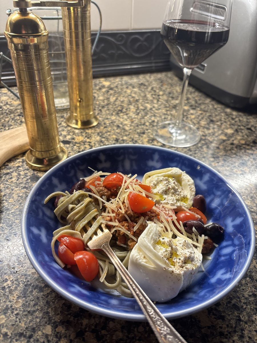 A plated pasta with burrata, tomatoes and olives